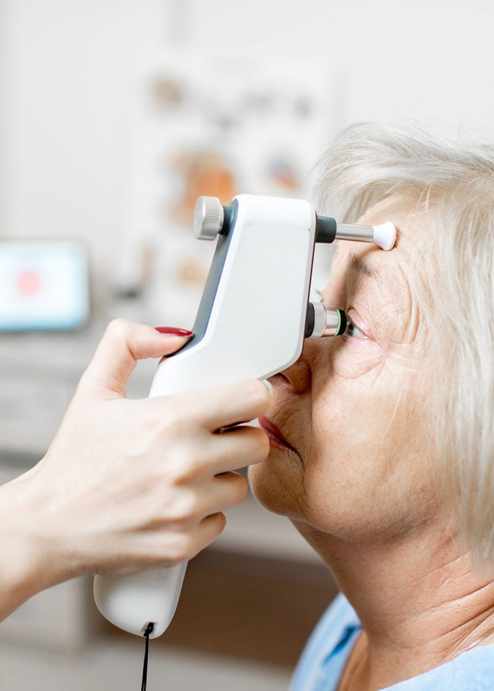 Doctor measuring the eye pressure with modern tonometer to a senior patient in the medical office, close-up